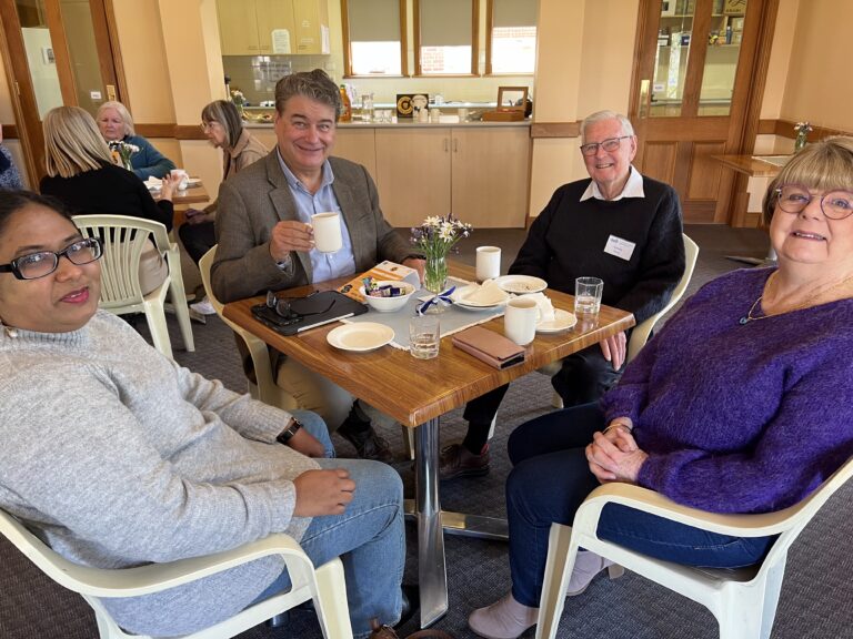 Four people sit around a table enjoying morning tea